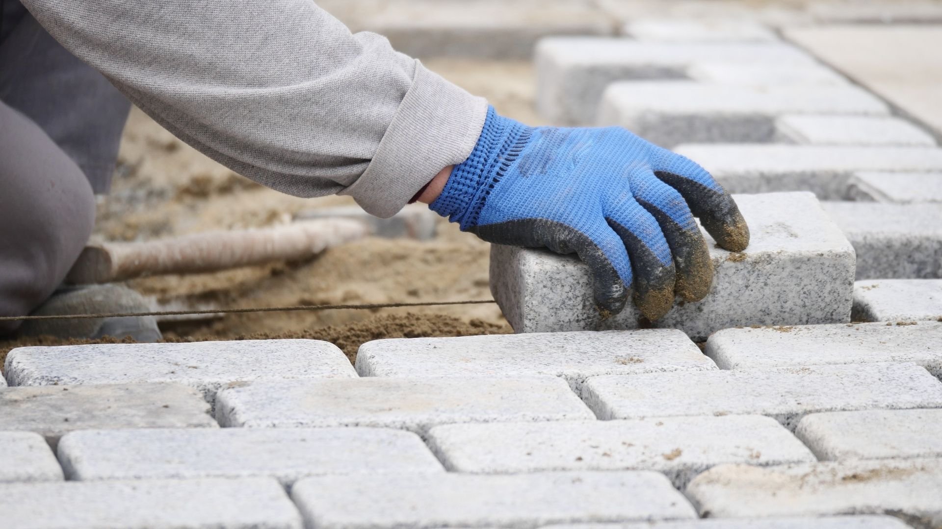 Worker with blue gloves laying pavers for lawn care landscaping project