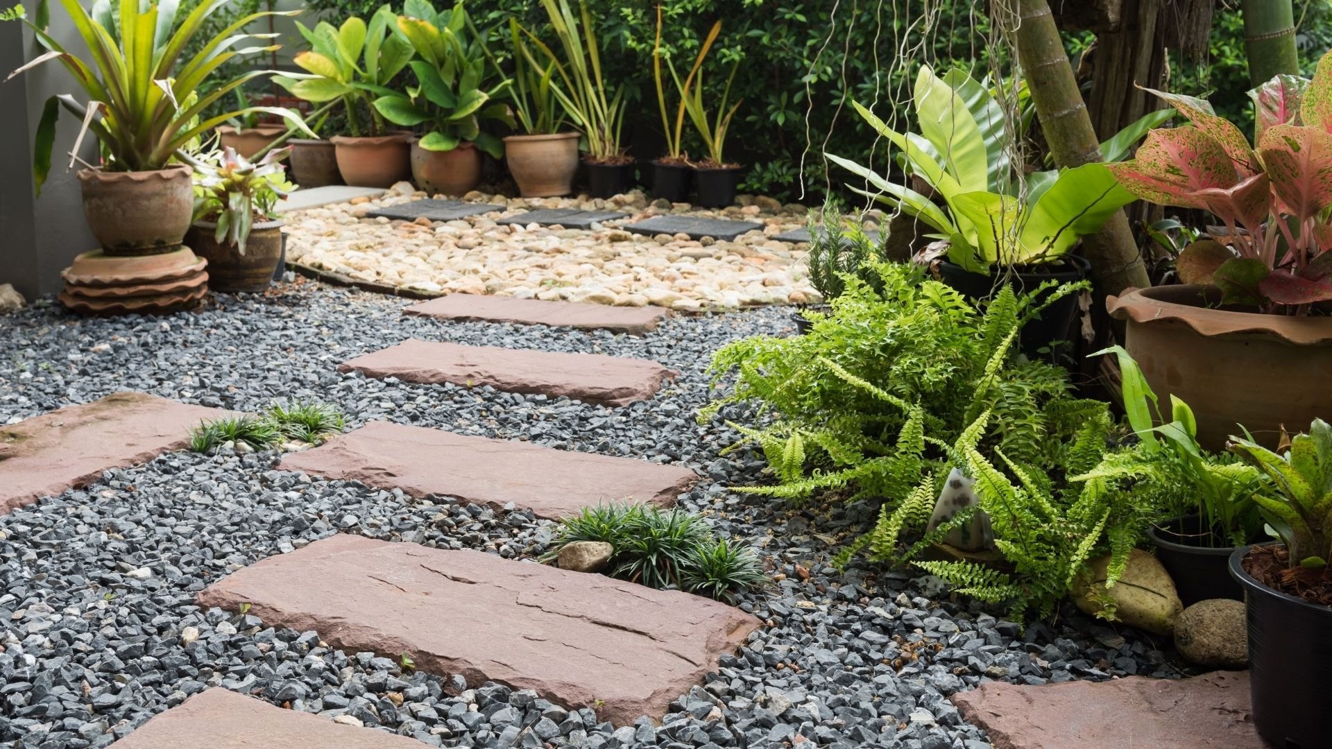 Landscaped garden with stone pathway, gravel, potted plants, lawn care design